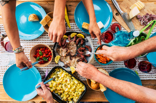 Vertical view of a group of friends or family eating together. Friendship and celebration at lunch time with food. People enjoying meal taking from dishes. Concept of nutrition and social real life - Фото, изображение
