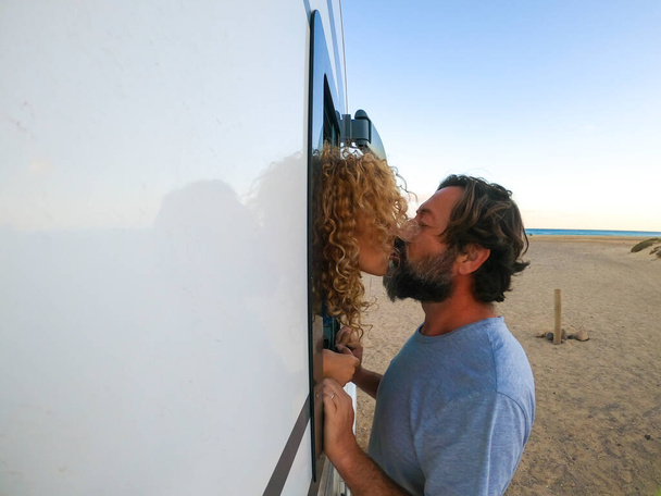 Yetişkin erkek ve kadın yaz tatili boyunca öpüşüyor. Olgun bir adam karavanın dışında karısını öpüyor. Sahilde bir yolculuk yeri. Aşık insanlar göçebe yaşam tarzından zevk alıyorlar. - Fotoğraf, Görsel