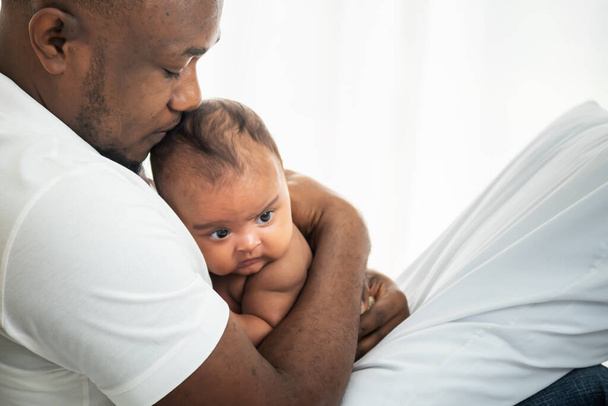 Afroamerykański ojciec całuje głowę swojemu 3-miesięcznemu nowonarodzonemu synowi, ze szczęściem i ochroną, koncepcją dla afroamerykańskiej rodziny i noworodka - Zdjęcie, obraz
