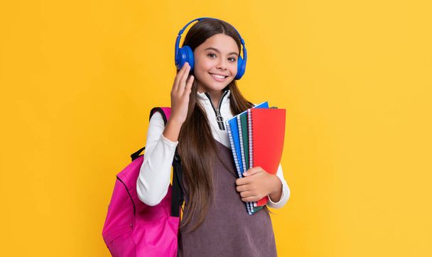 child smile in headphones with school backpack with workbook on yellow background - Photo, image