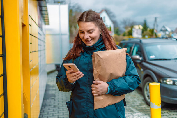 Mladá běloška dostává balíček z buňky automatického poštovního terminálu venku.  - Fotografie, Obrázek