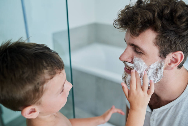 Anna minun tehdä se puolestasi, isä. Laukaus pieni poika hankaa partavaahtoa hänen isänsä kasvot kylpyhuoneessa kotona. - Valokuva, kuva