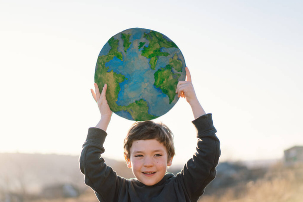 Mały chłopiec trzymający planetę w rękach na zielonym tle wiosny. Dzień Ziemi - Zdjęcie, obraz