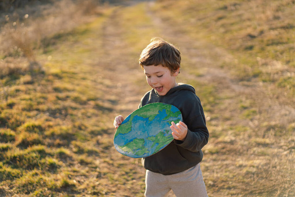 Niño pequeño sosteniendo el planeta en las manos contra el fondo verde de primavera. Día de la Tierra - Foto, Imagen