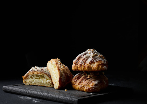 pečené croissanty na černé dřevěné desce posypané práškovým cukrem - Fotografie, Obrázek
