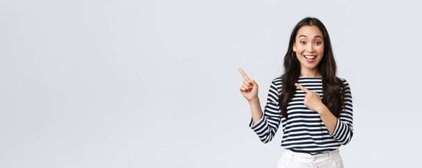 Styl życia, ludzkie emocje i luźna koncepcja. Przystojny młody koreański kobieta reklamować produkt, uśmiechnięty aparat podekscytowany i wskazując palce w lewym górnym rogu na baner promo - Zdjęcie, obraz