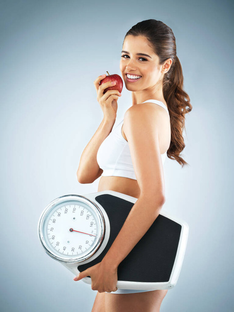 Zdraví je o tvých zvycích. Studio portrét atraktivní mladé ženy držící jablko a měřítko na šedém pozadí. - Fotografie, Obrázek