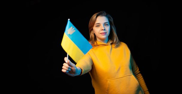 Ukraine national flag. Beautiful ukrainian girl with government flag on a stick in her hands on black background. Symbol of Ukrainian statehood - Фото, зображення