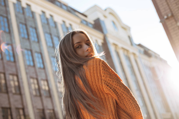 Blonde woman looking at camera over the shoulder. pretty female model dressed in red sweater posing on the sunset city street - Fotoğraf, Görsel