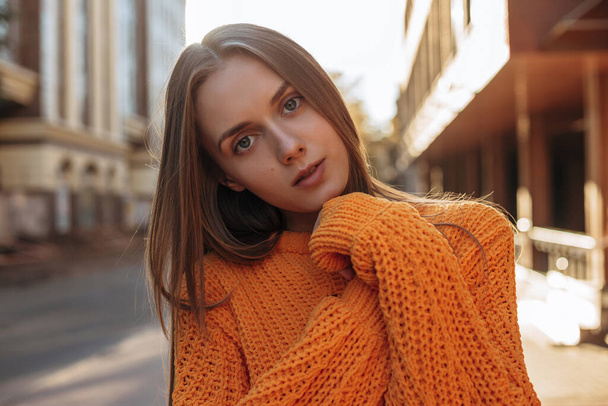 tenera giovane donna in posa e guardando la fotocamera. modello vestito in maglione arancione a maniche lunghe  - Foto, immagini