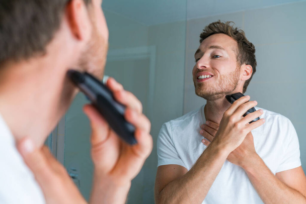 Young man shaving neck and jawline in the morning using electric shaver clipper. Morning routine modern lifestyle. Male beauty 30s model - Fotó, kép