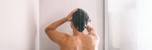 Shower man washing hair rinsing shampoo in bathroom banner panorama. Showering person at home lifestyle. Young guy taking a shower - 写真・画像