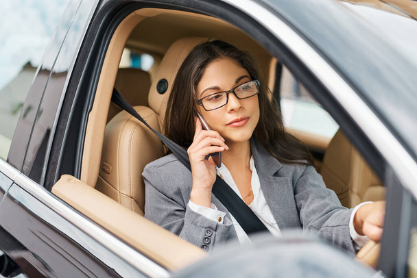 Informiert ihre Kollegen, die auf ihrem Weg sind. Aufnahme einer Geschäftsfrau, die während der Fahrt mit ihrem Auto telefoniert. - Foto, Bild