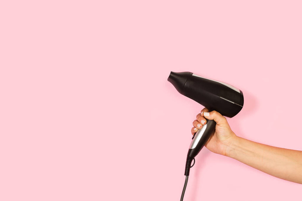 Woman hand holding a hair dryer on a pink background with copy space - Photo, Image