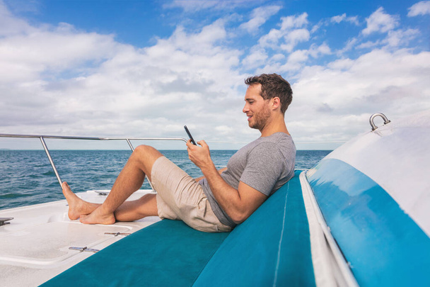 Barca uomo utilizzando il telefono cellulare sms su internet satellitare mentre rilassarsi sul ponte di yacht stile di vita di lusso - Foto, immagini