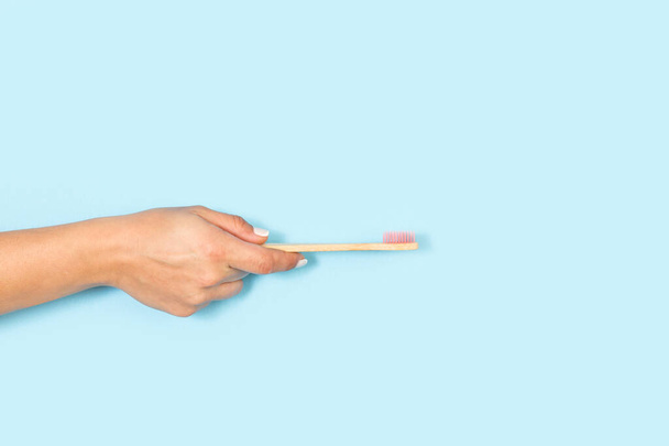 Cepillo de dientes de bambú de mano de mujer sobre un fondo azul claro con espacio para copiar - Foto, imagen