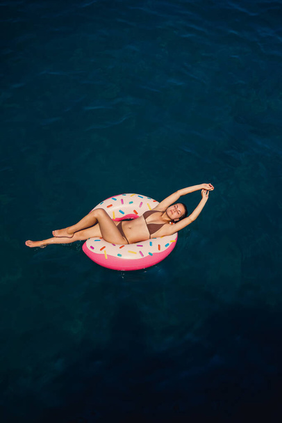 Une jeune femme en maillot de bain nage sur un anneau gonflable dans la mer. Concept vacances d'été. - Photo, image