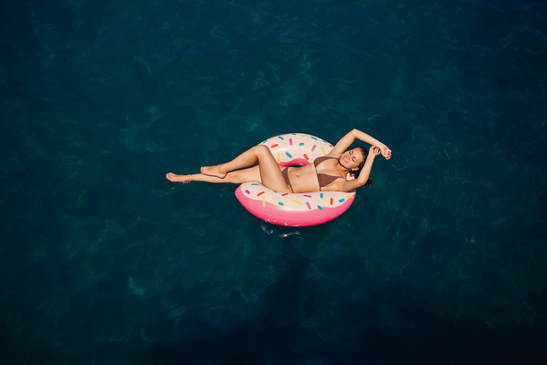 Young woman in a swimsuit swims on an inflatable ring in the sea. Summer vacation concept. - Foto, Imagen