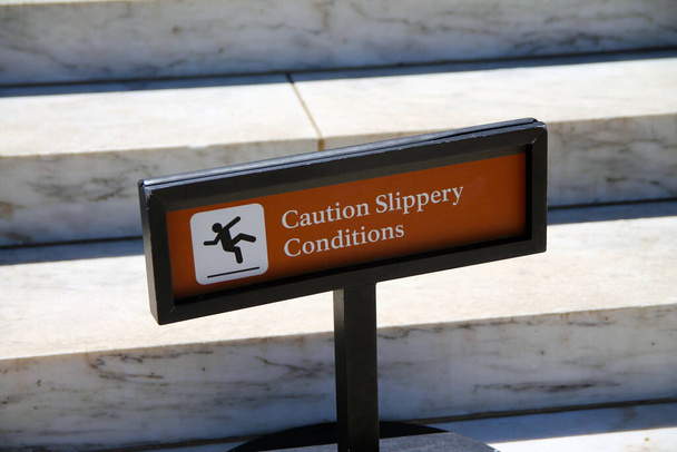 Caution, slippery conditions brown sign with icon representation on marble steps with a black holder on a sunny day - Photo, Image