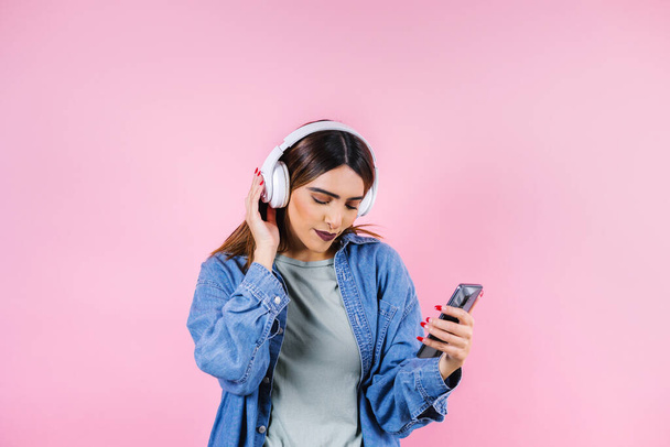 mujer joven hispana con auriculares, bailando y escuchando música sobre fondo rosa en América Latina - Foto, imagen