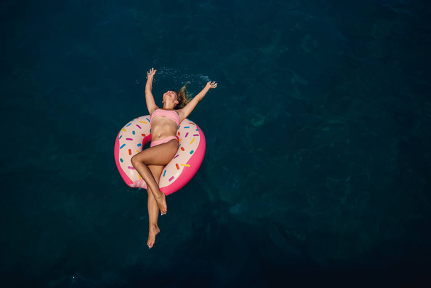 Une jeune femme en maillot de bain nage sur un anneau gonflable dans la mer. Concept vacances d'été. - Photo, image
