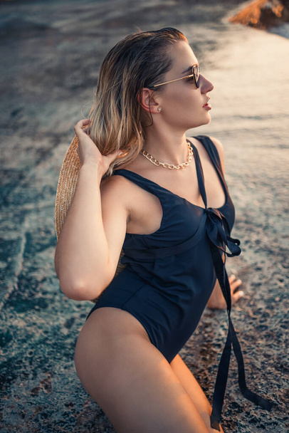 Young woman in sunglasses is resting at the sea slender in a black swimsuit. Selective focus - Photo, Image