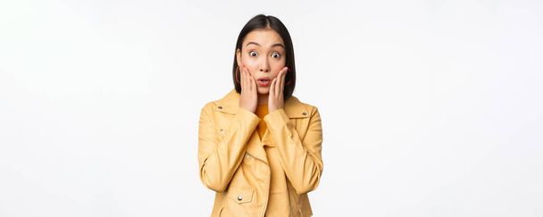 Image of asian woman looking surprised, amazed reaction, shocked face, standing over white background - Φωτογραφία, εικόνα