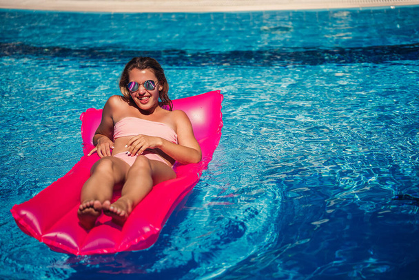 Seksowna modelka odpoczywająca i opalająca się na materacu w basenie. Kobieta w różowym bikini unosząca się na dmuchanym różowym materacu. spf i filtry przeciwsłoneczne - Zdjęcie, obraz