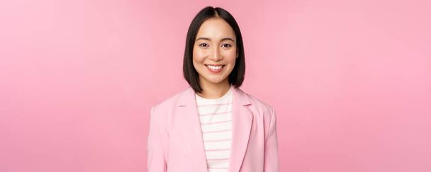 Junge Fachkräfte. Lächelnde asiatische Geschäftsfrau, Verkäuferin im Anzug schaut selbstbewusst in die Kamera, posiert vor rosa Hintergrund - Foto, Bild