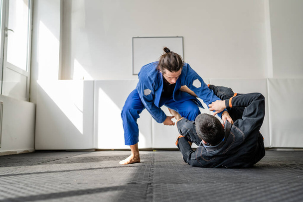 Dois atletas brasileiros de jiu jitsu BJJ treinando na academia de artes marciais chão lutando sparring desgaste kimono gi esporte uniforme no tatami tapetes esportes jiujitsu e autodefesa conceito espaço de cópia - Foto, Imagem
