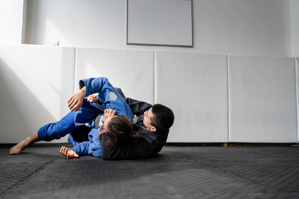 Two brazilian jiu jitsu BJJ athletes training at the academy martial arts ground fighting sparring wear kimono gi sport uniform on the tatami mats sports jiujitsu and self-defense concept copy space - Photo, Image