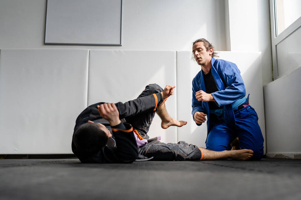 Dois atletas brasileiros de jiu jitsu BJJ treinando na academia de artes marciais chão lutando sparring desgaste kimono gi esporte uniforme no tatami tapetes esportes jiujitsu e autodefesa conceito espaço de cópia - Foto, Imagem