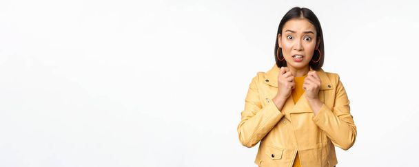Image of scared asian woman looking insecure and worried at camera, gasping shocked, standing worried against white background - Photo, Image