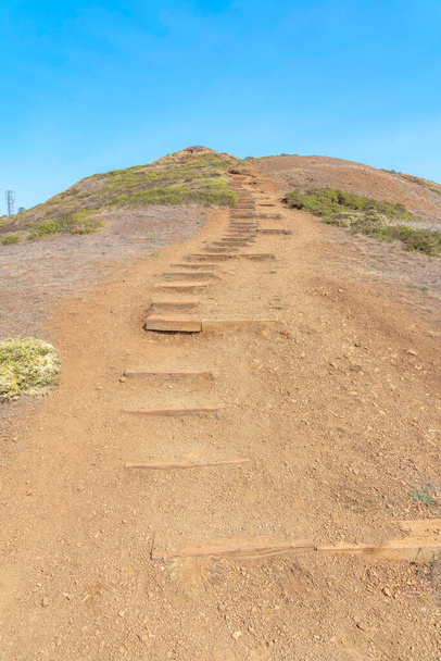 Mountain trail with wooden steps on the slope at the view from Twin Peaks in San Francisco, CA. Low angle view of a dry slope with grass near the top against the clear blue sky. - Fotografie, Obrázek