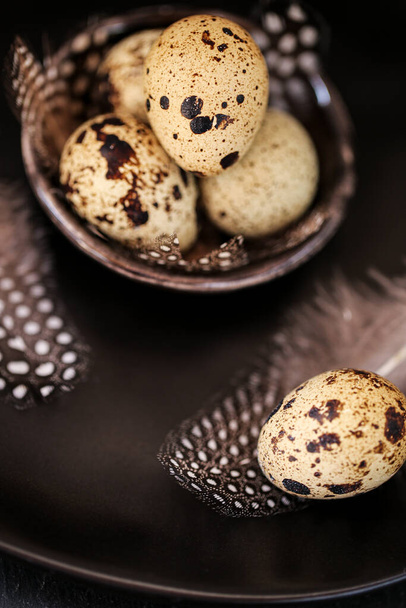Quail eggs with feathers in a black plate on a black slate background.Organic Farm natural quail eggs set.natural protein.Useful healthy food and products - Zdjęcie, obraz