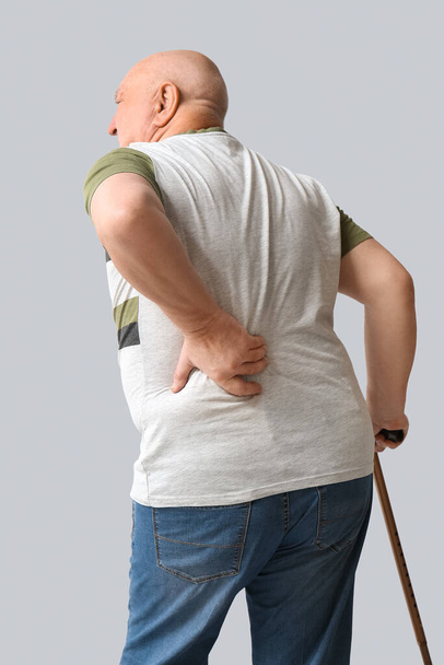 Homem sênior com bengala sofrendo de dor nas costas no fundo claro - Foto, Imagem