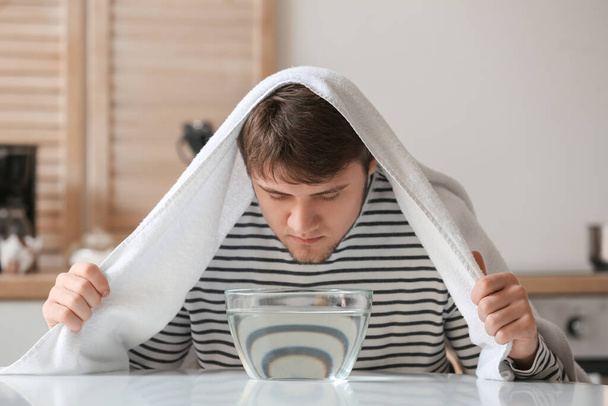 Молодой человек вдыхает пар дома, чтобы успокоить и открыть носовые проходы - Фото, изображение