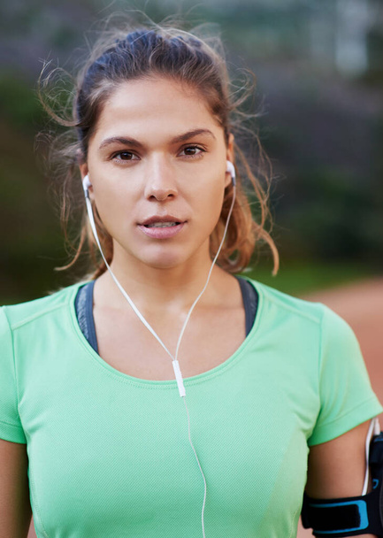 Cant wait to hit the trail. Shot of a young woman listening to music while out running. - Фото, изображение