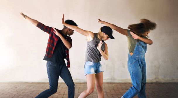 Ballare fa parte della nostra vita. Colpo ritagliato di un giovane gruppo eterogeneo di ballerini che eseguono una routine contro uno sfondo murato all'aperto. - Foto, immagini