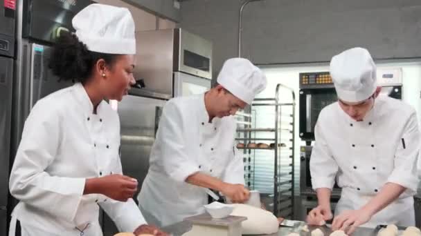 Multiracial professional gourmet team, three chefs in white cook uniforms and aprons knead pastry dough and eggs, prepare bread, and bakery food, baking in oven at stainless steel restaurant kitchen. - Filmagem, Vídeo