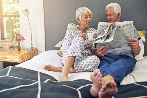 Η ανάγνωση εφημερίδας ενισχύει τη χαλάρωση. Πυροβολισμός ενός ηλικιωμένου ζευγαριού ξαπλωμένου στο κρεβάτι. - Φωτογραφία, εικόνα