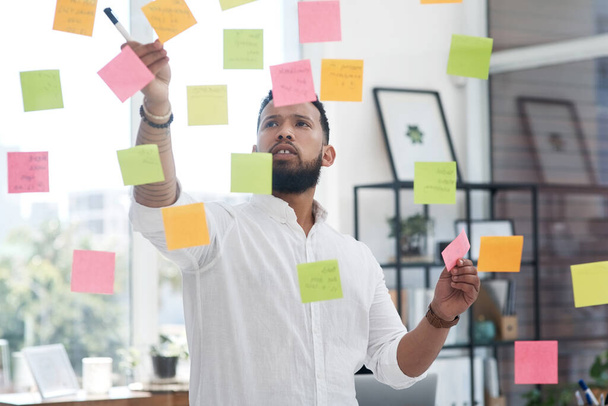 Play around with your ideas and see where they lead. Shot of a young businessman brainstorming with sticky notes on a glass wall in an office. - Foto, Imagen