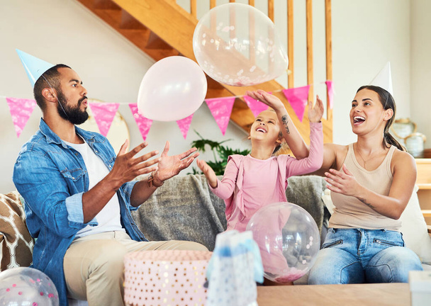 Mehr Luftballons machen es zu einer richtigen Party. Aufnahme eines kleinen Mädchens, das zu Hause mit seinen Eltern Geburtstag feiert. - Foto, Bild