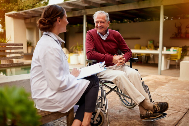 Son buenas noticias, doc. Fotografía de un joven médico y su paciente mayor hablando mientras estaba sentado afuera. - Foto, imagen