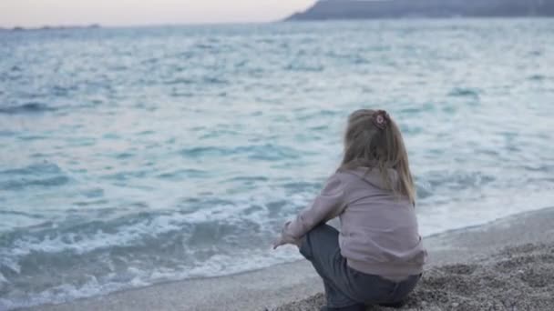 Ребенок сидит у моря на закате - Кадры, видео
