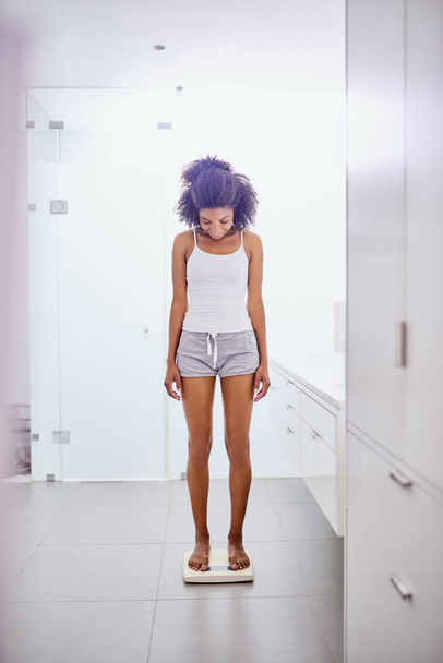 Now thats what I like to see. Shot of an attractive young woman weighing herself on a scale in the bathroom at home. - Foto, afbeelding