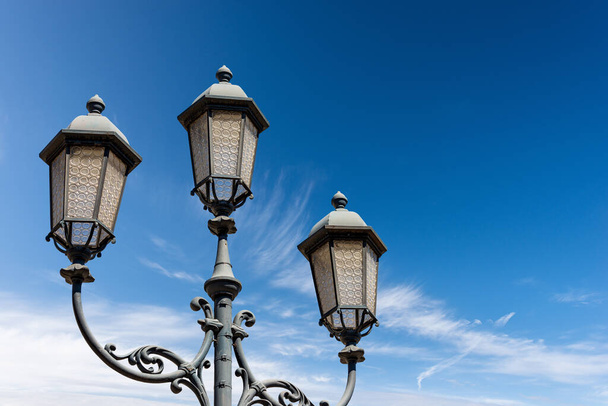 Close-up of old street lamp posts against a clear blue sky with clouds and copy space. Loggia town square (Piazza della Loggia), Brescia downtown, Lombardy, Italy, Southern Europe. - 写真・画像