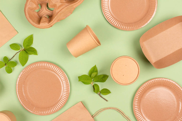 Flat lay composition with eco-friendly tableware and kraft paper food packaging on light green background. Sustainable packaging, recyclable paperware, sustainable food packaging concept. Selective focus - Photo, Image