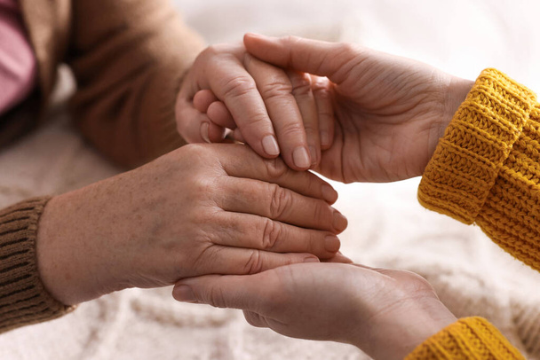 Young and elderly women holding hands together indoors, closeup - Foto, imagen