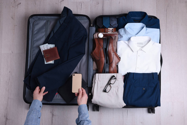 Man packing suitcase for business trip on wooden floor, top view - Photo, image